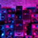 Many types of speakers stacked 4-5 speakers high in front of the brick wall with a blue and magenta light